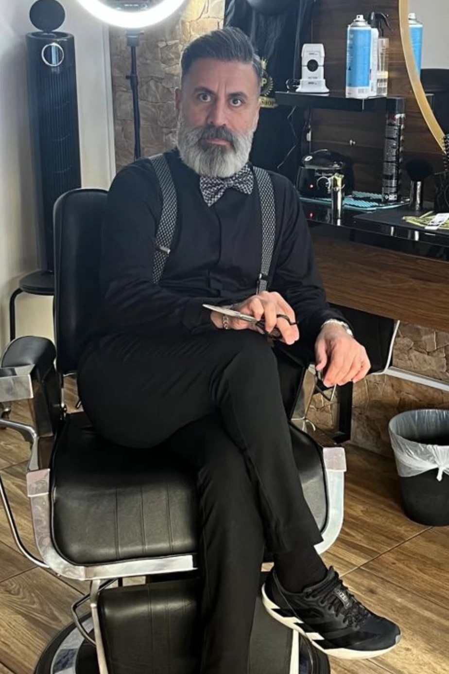 Frisören sitter i en av salongens svarta barberarstolar med saxen i handen