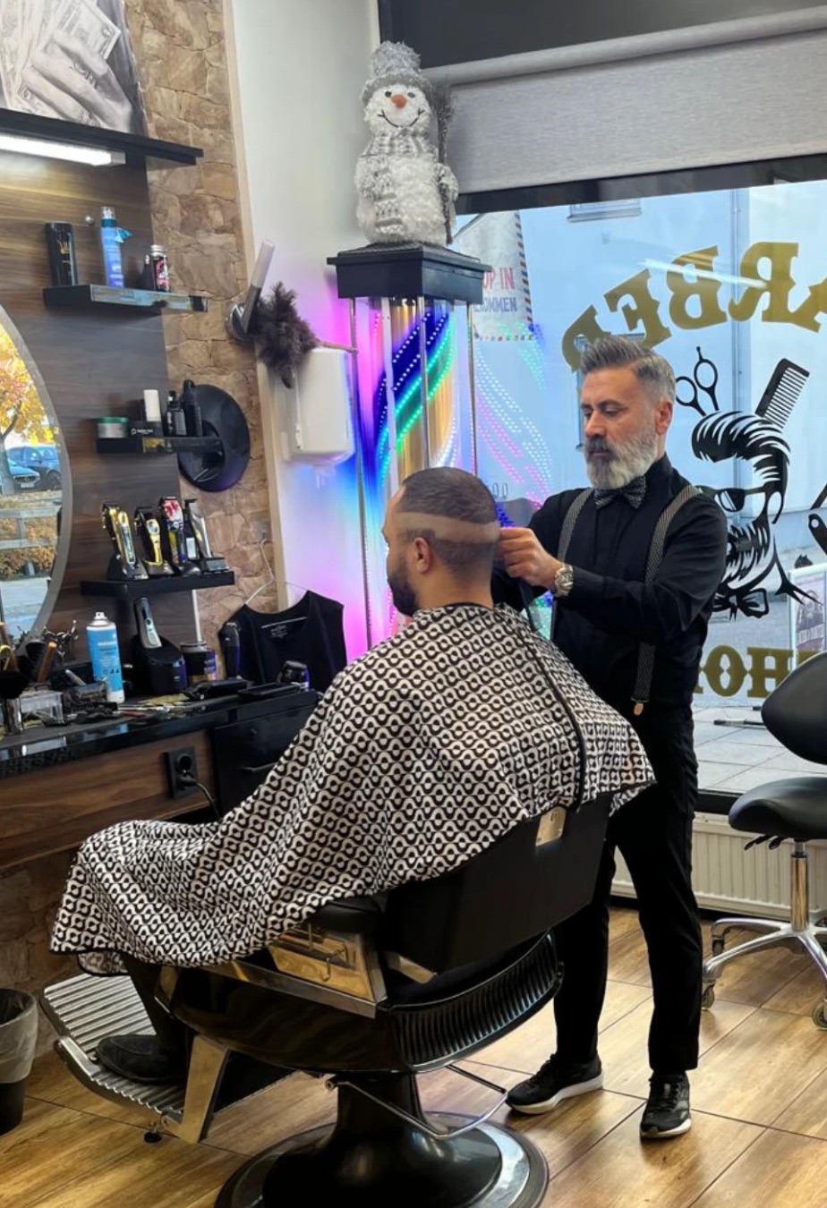 Frisören rakar in en skarp linje i en kunds fade framför barberarstolpen